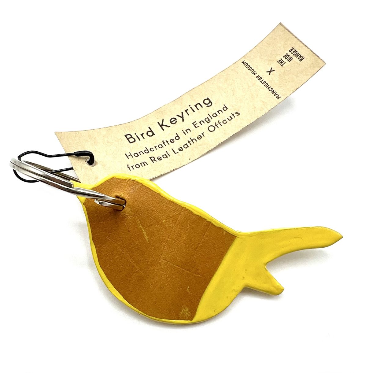 A bird shaped keyring of a sitting bird. The tail and wing tip is painted yellow and the same yellow is painted as an outline around it's body. The keyring is where the eye would be and a paper swing tag is fastened to the keyring with a black safety pin. Tag text: Bird keyring. Handcrafted in England from real leather offcuts.