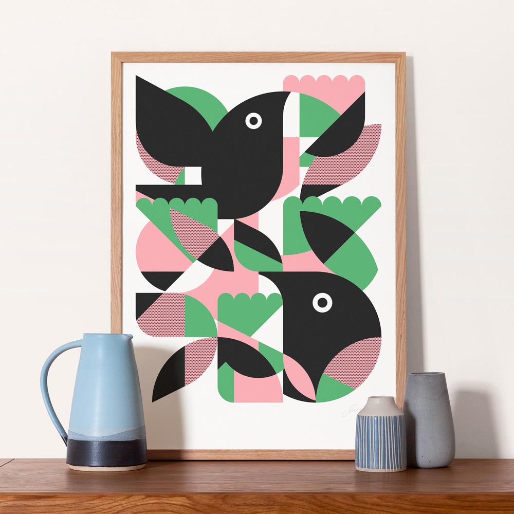 Framed abstract art print in black, pink, and green shapes on a white background, displayed on a wooden surface with decorative vases.