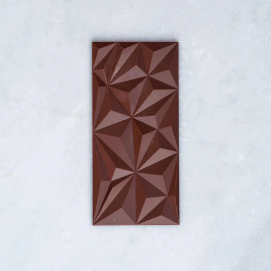 Dark chocolate bar with geometric patterns across the top, placed on a light grey background.