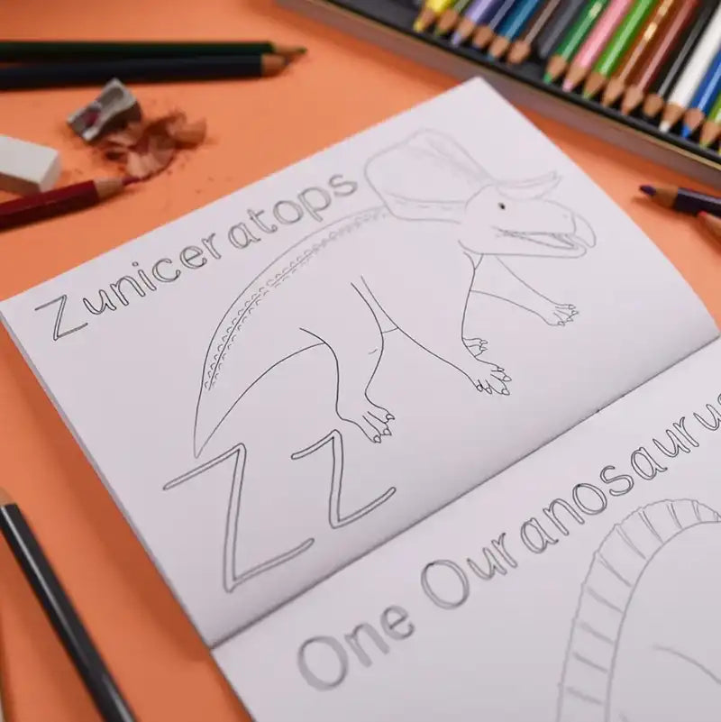 Inside page of a colouring book featuring an outline of a Zuniceratops placed on an orange table surrounded by stationery