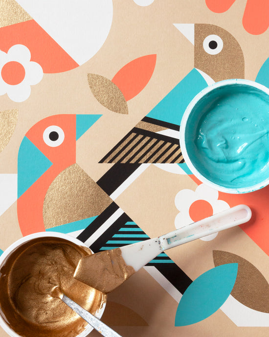 Two bowls of gold and blue paint with a paintbrush on a colorful abstract background