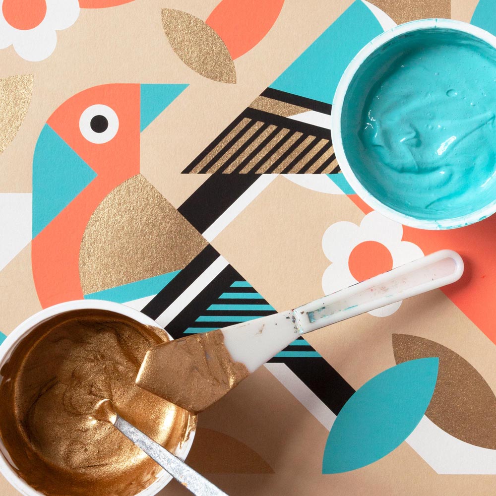 Two bowls of gold and blue paint with a paintbrush on a colourful abstract background