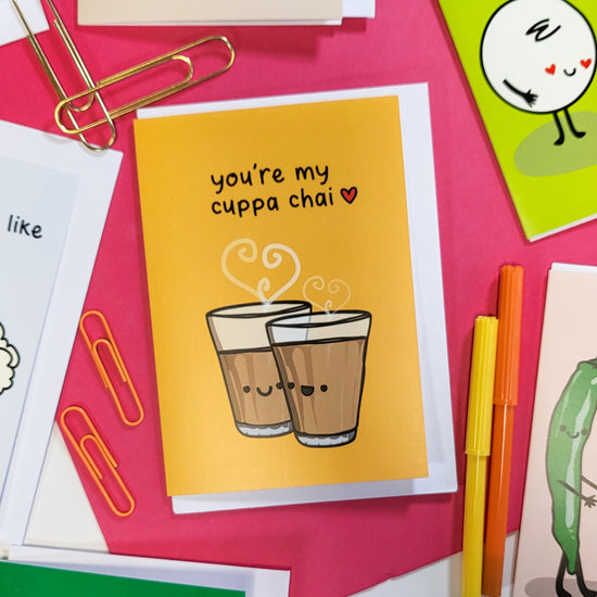 A greeting card with a bright yellow background featuring two cute, anthropomorphic chai tea cups with hearts above them. The text "You're my cuppa chai" is written in bold letters below the cups.