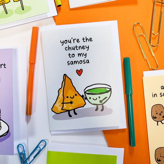 Greetings card with an illustration of samosa and chutney hugging on a desk with some stationery around it