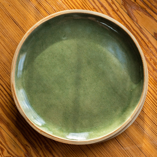 Handmade plate made with a green glaze - with unglazed rim. Photographed birds eye view on a wooden table.