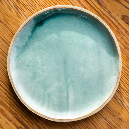 Handmade plate made with a turquoise glaze - with unglazed rim. Photographed birds eye view on a wooden table.