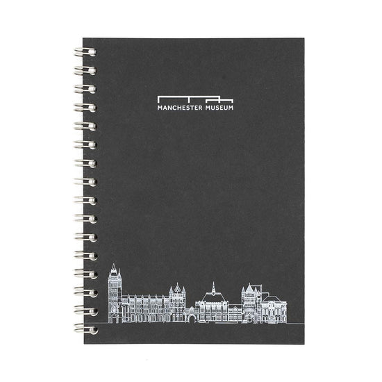 Wirobound black notebook photographed against a white background from a birds eye view. The notebook has Manchester Museum's logo at the top centre in silver, and a silver line drawing of Manchester Museum at the bottom centre.