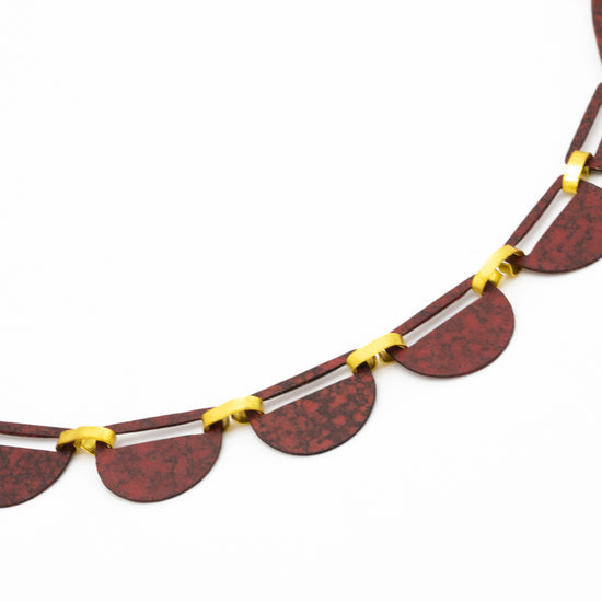 Close up of a necklace comprising of a number of red semi-circles bound together with gold fastenings. Photographed against a white background.
