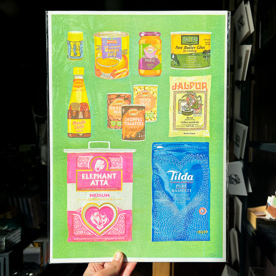 A person holding up a print illustration filled with Desi Pantry items 