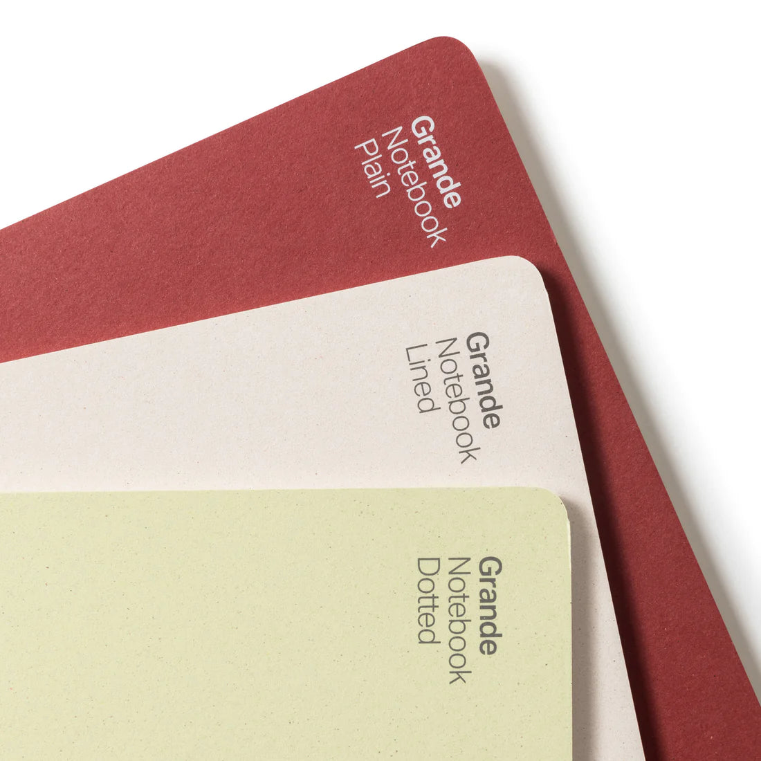 Detail of thee notebooks (one red, one white, one yellow) placed on top of each other in front of white background.