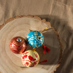 3 Baubles photographed from a birds-eye view sat on a circular tree trunk chopping board.
