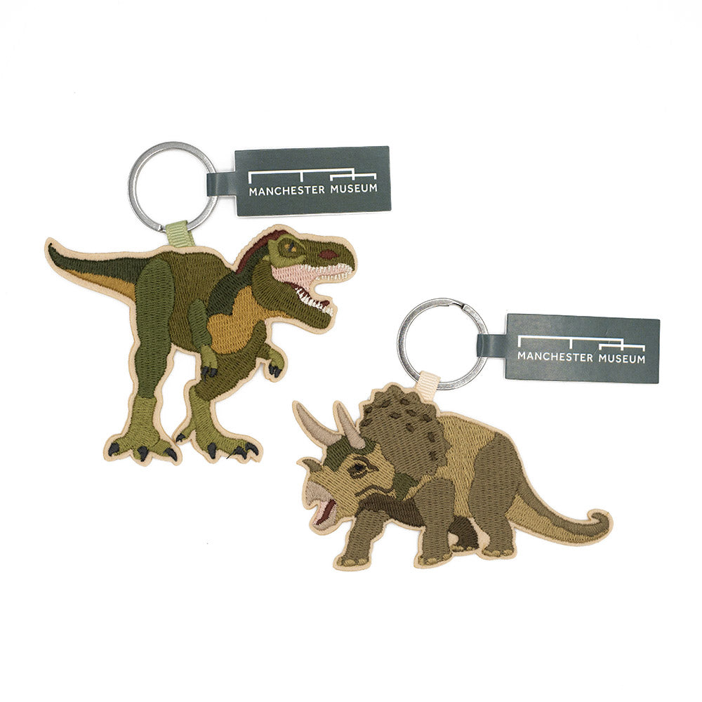 Two dinosaur keychains with Manchester Museum labels on a white background