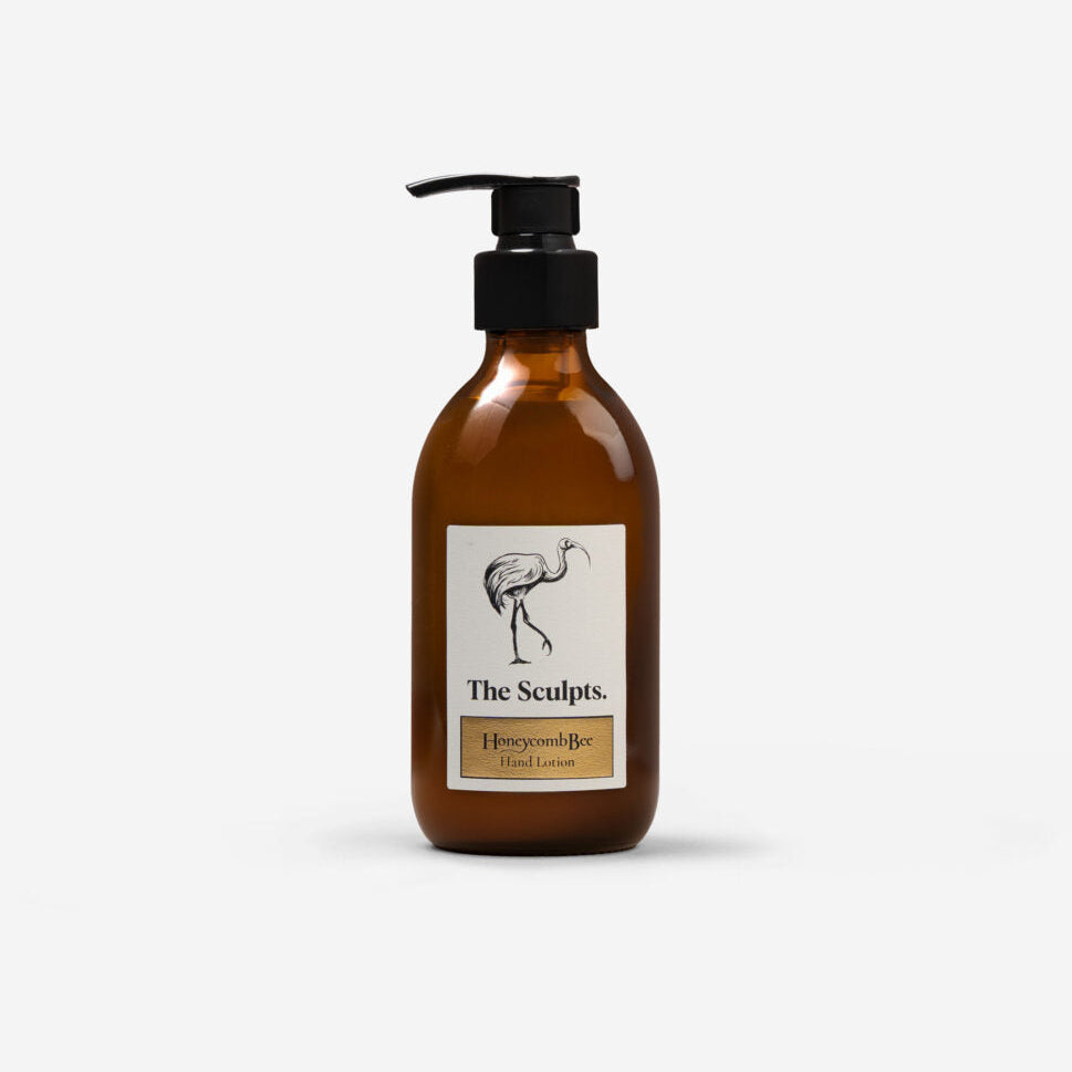 An amber glass pump bottle with a black dispenser cap and a cream label featuring a black flamingo illustration and the text 'The Sculpts. Honeycomb & Hand Lotion'.
