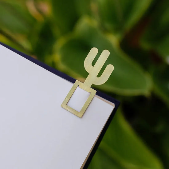 The image shows a gold bookmark shaped like a cactus, marking a page in a book.