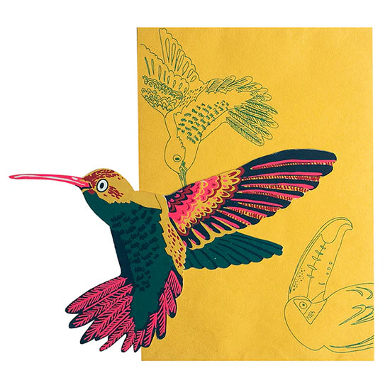 Orange-yellow envelope with a hummingbird and toucan outline on it and on top is a hummingbird shaped card in green, pink and yellow.