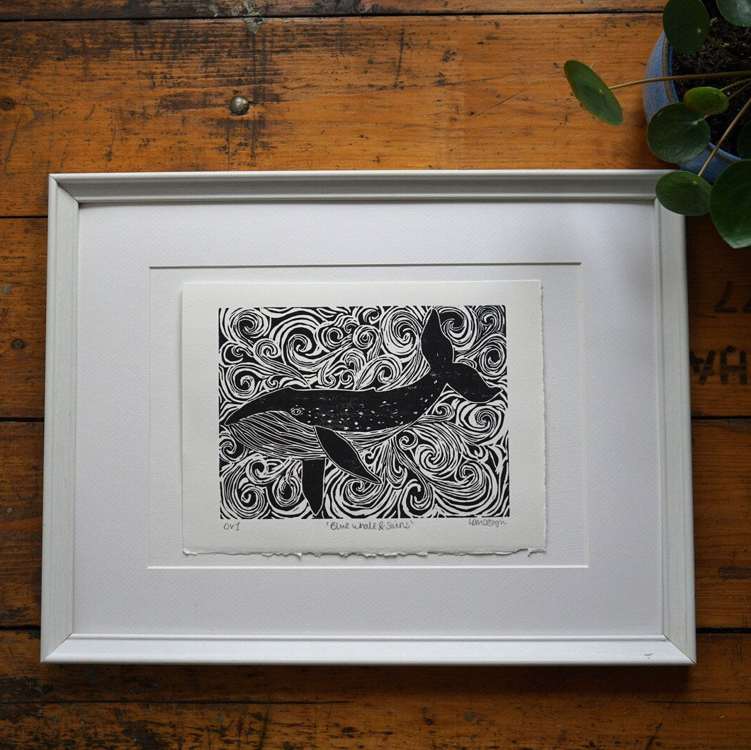Framed black and white artwork of a blue whale on a wooden surface