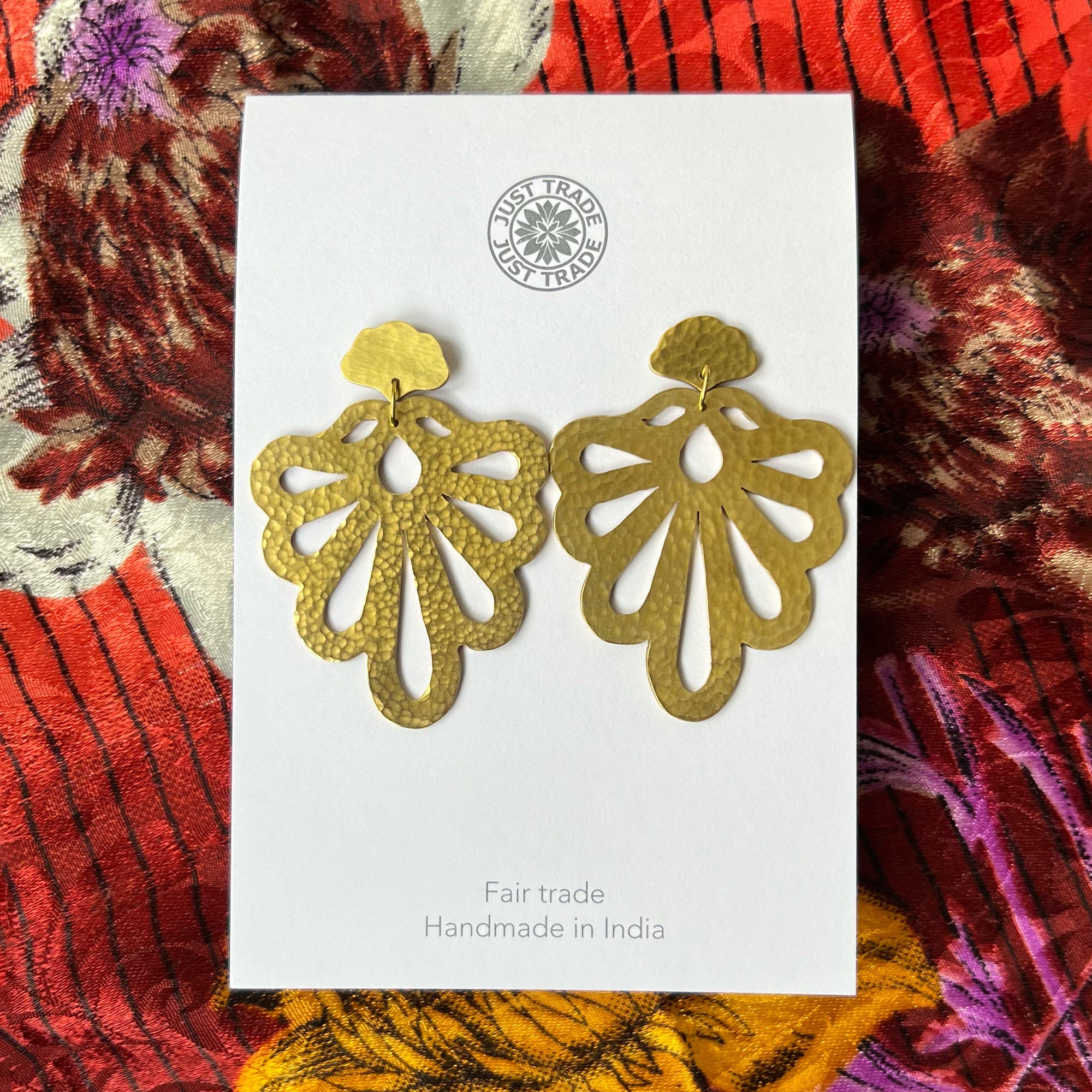 Lobed cutout earrings in an upside down fan shape against a colourful patterned fabric background.