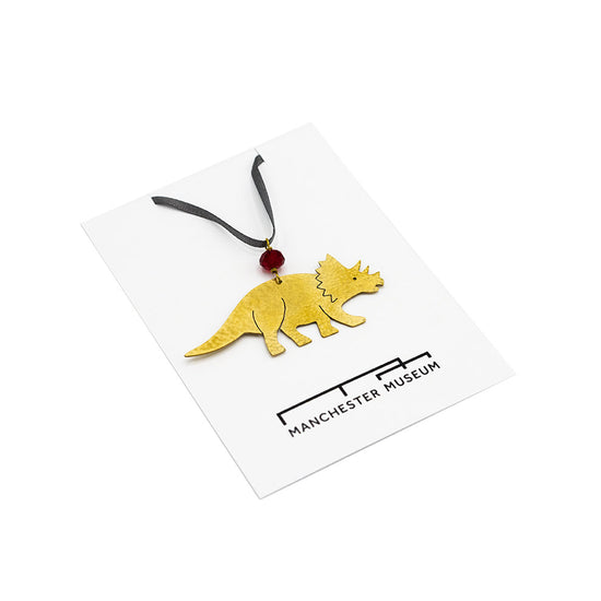 Load image into Gallery viewer, Hammered brass decoration in the shape of a Triceratops photographed against Manchester Museum branded backing card 
