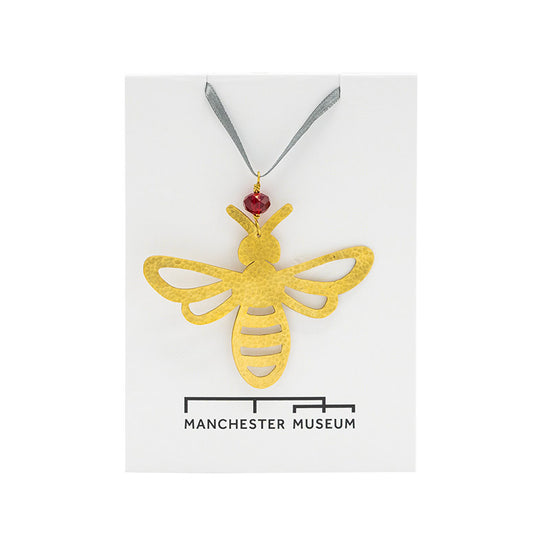 bee decoration made with hammered brass photographed on top of Manchester Museum branded backing card