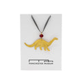 Hammered brass decoration in the shape of a Diplodocus photographed against Manchester Museum branded backing card