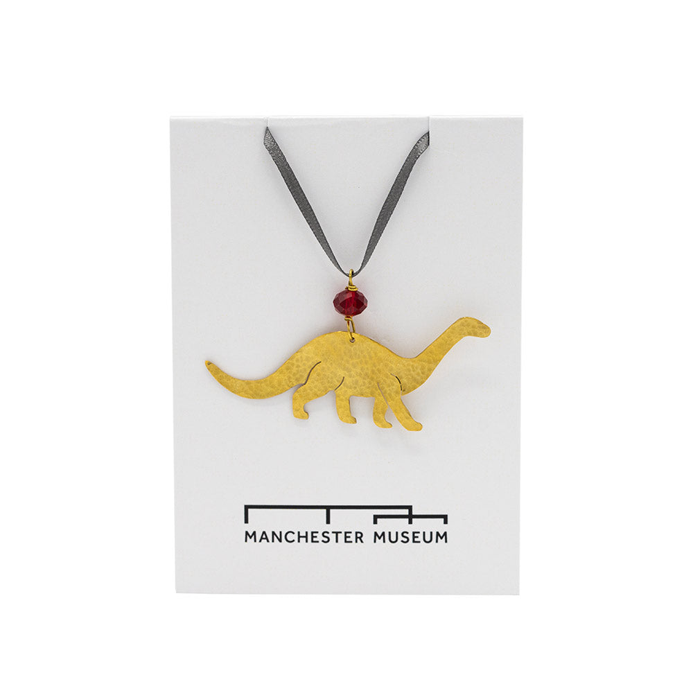 Hammered brass decoration in the shape of a Diplodocus photographed against Manchester Museum branded backing card