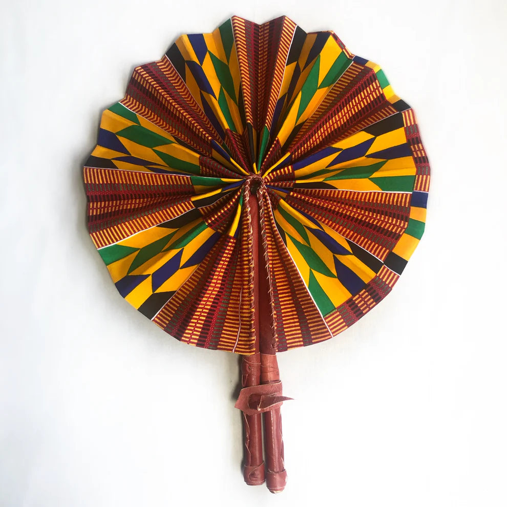 Kente fan fully folded out, lying on white backdrop.