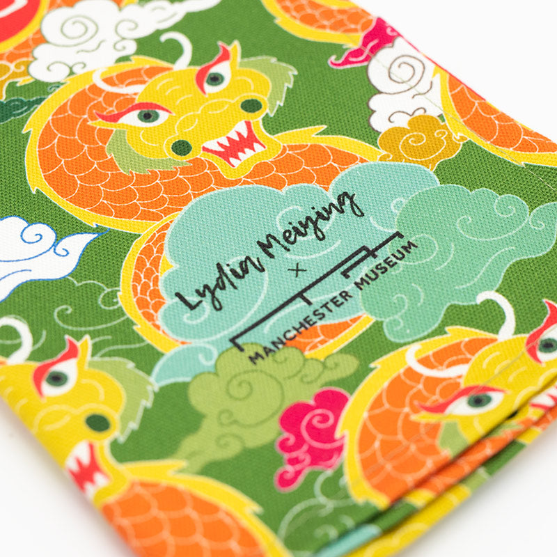Load image into Gallery viewer, Close up of Lydia Meiying and Manchester Museum logo on a tea towel with a green, yellow, orange, and red dragon print

