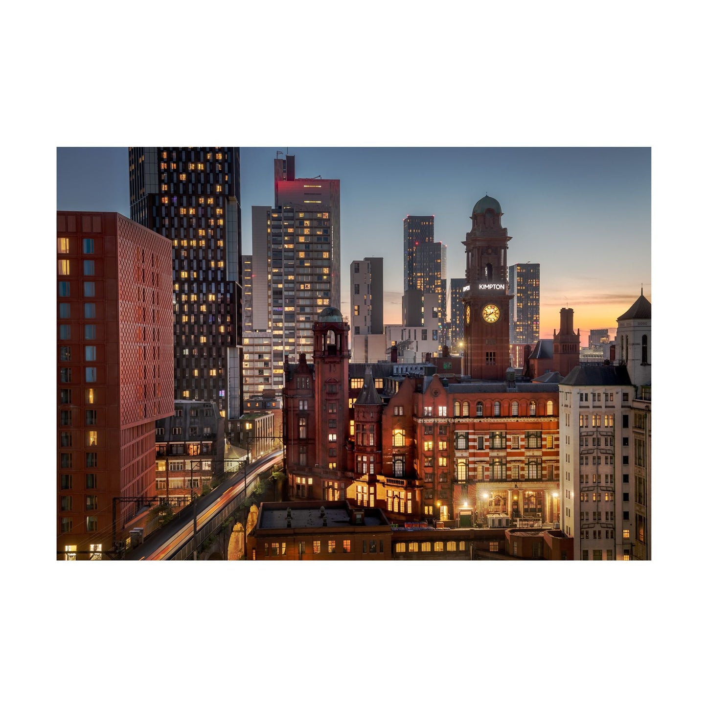 Load image into Gallery viewer, Simon Buckley photography of the Manchester skyline seen towards the Principal. The scene is a sunset or early morning with lights shining form the windows and soft peach and orange hues in the background of the sky.
