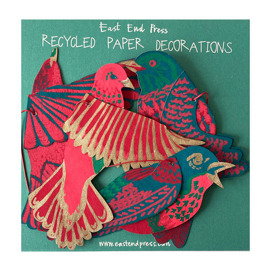 Various coloured birds made out of recycled paper against green backing card.