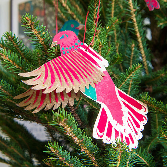 Pink bird made out of recycled paper, hung on a Christmas tree.