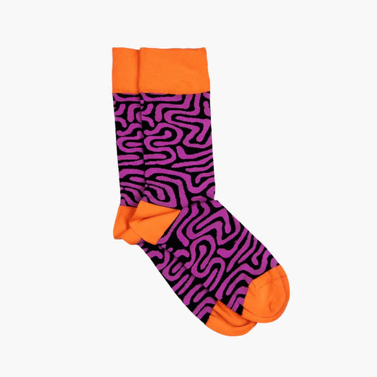 Socks against white background. Vibrant pueple and black pattern design. The toes, heals and tops of the socks are a bright orange.