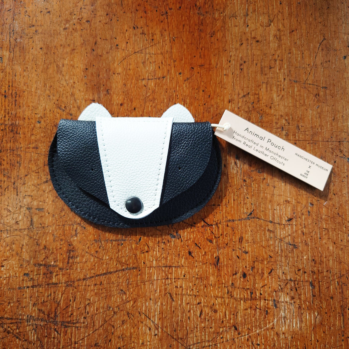 Recycled leather purse in the shape of a badger's face against a wooden surface.