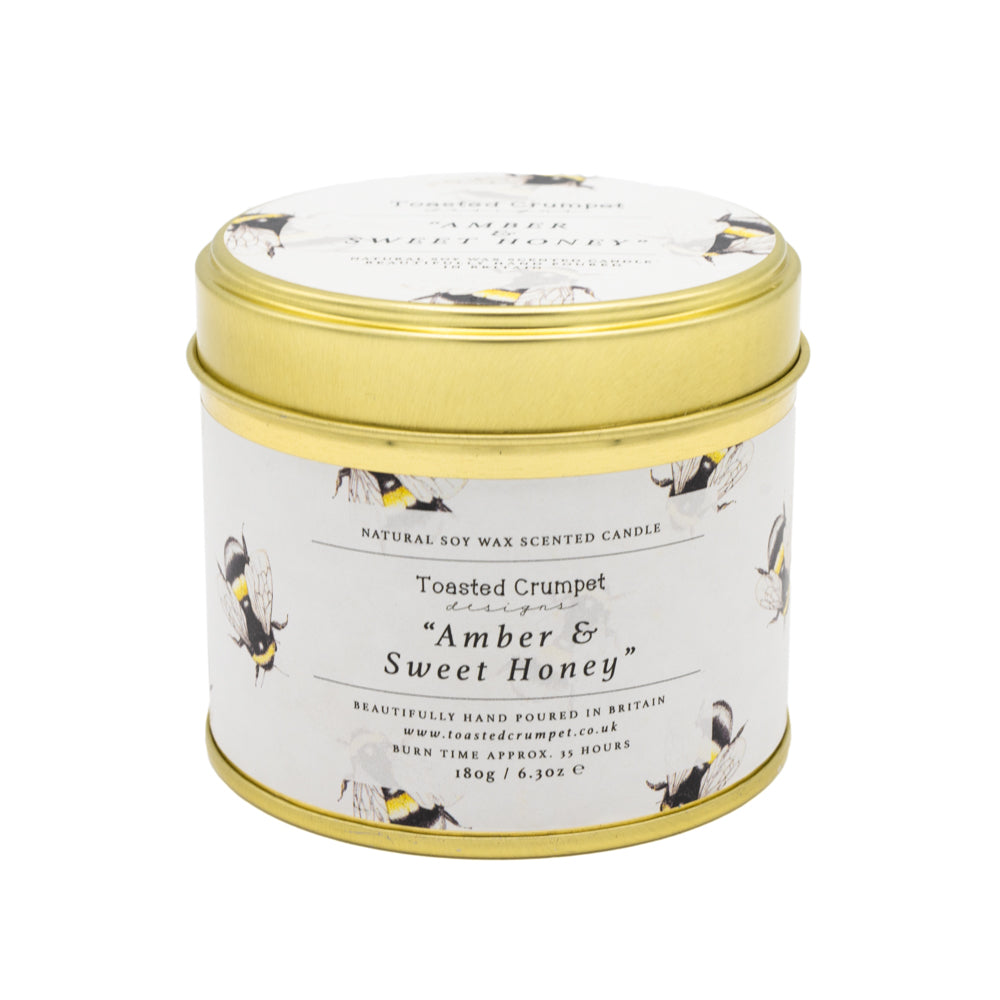 Candle in gold tin with bee pattened design label - white background. 