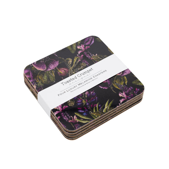Stack of 4 coasters with purple and black floral design. White belly band with Toasted Crumpet branding. White background.