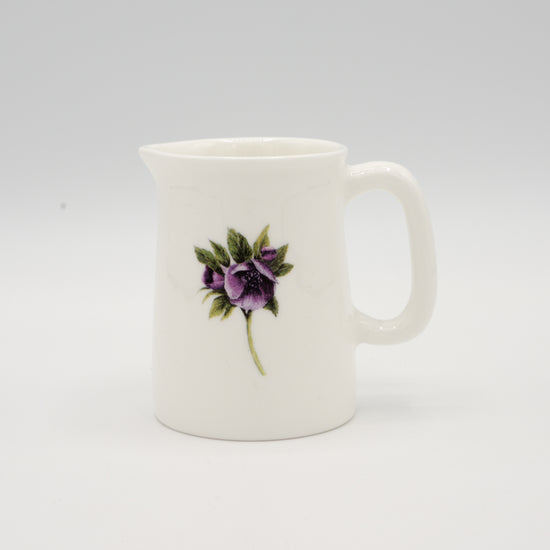 White jug with an illustration of a hellebore flower, photographed in front of a light grey background