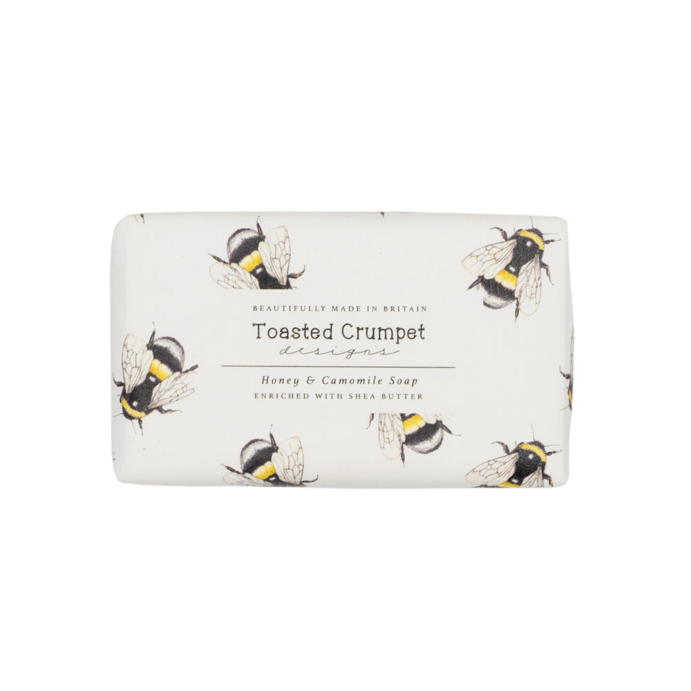 Rectangular soap in white packaging with a bee pattern. Photographed against white background.