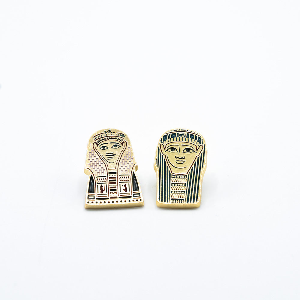 Two versions of the golden mummies pin shown side by side with the golden and red on the left and the golden and blue on the right.