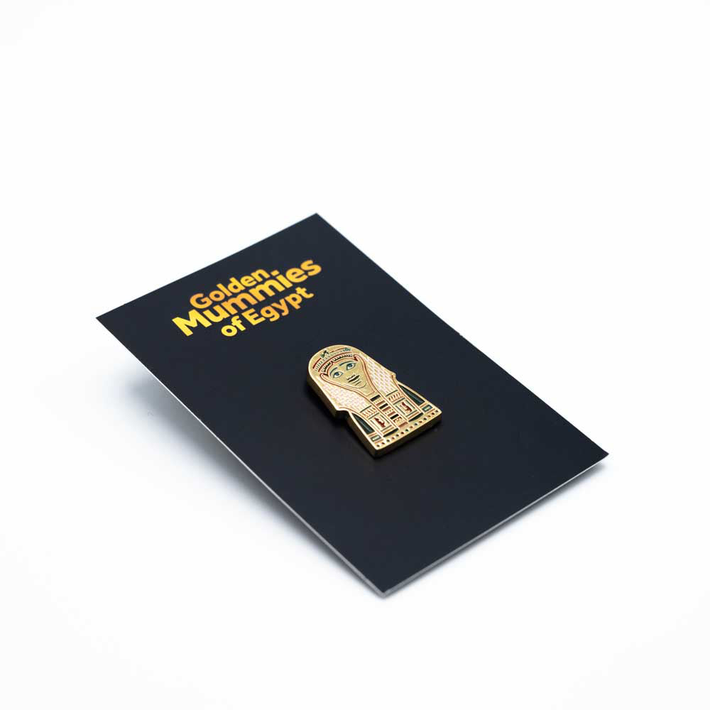 Golden pin with red engravings on a black backing card with the text, Golden Mummies of Egypt.