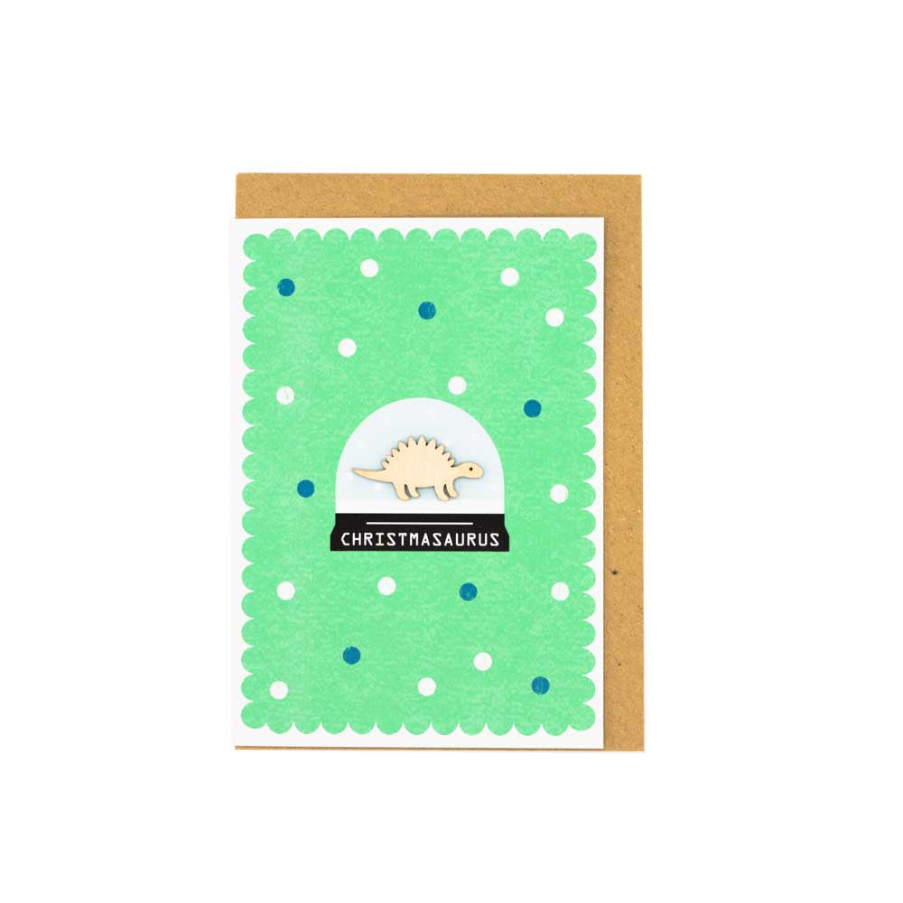 Load image into Gallery viewer, Image of a card with a brown envelope tucked inside. White background. Card is green with a wooden dinosaur decoration at the centre of a snowglobe. 
