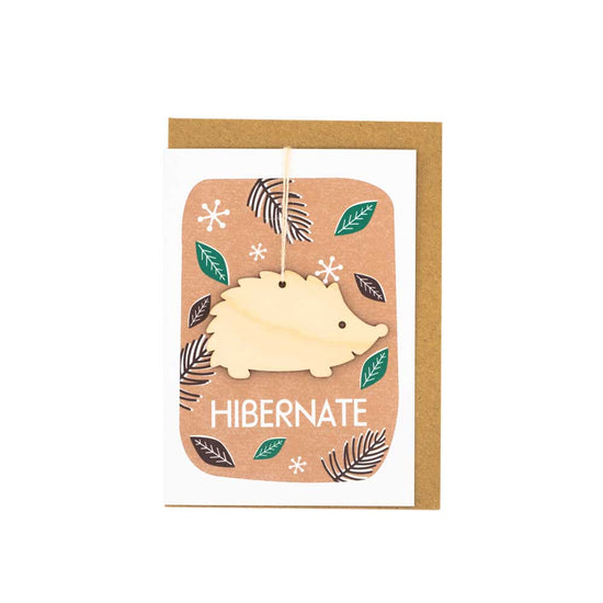 Card with brown envelope tucked inside, white background. Wooden hedgehog decoration against an autumnal background with the word 'Hibernate' at the bottom.