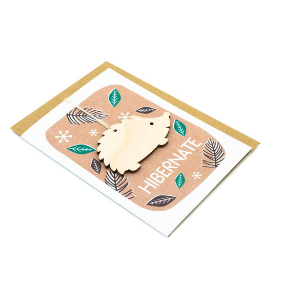 Card with brown envelope tucked inside, white background. Wooden hedgehog decoration against an autumnal background with the word 'Hibernate' at the bottom.