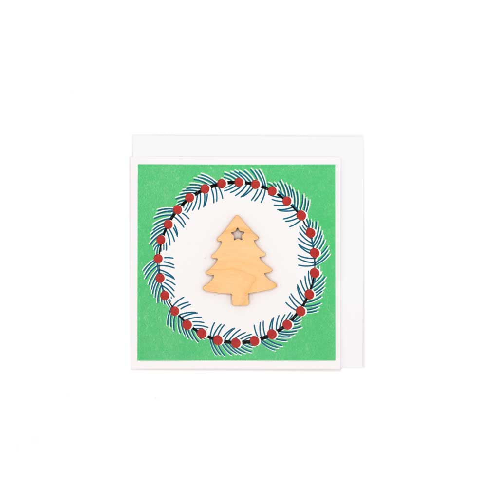 Square card with white envelope tucked inside, white background. Wooden Christmas Tree decoration at the centre of a Christmas wreath.
