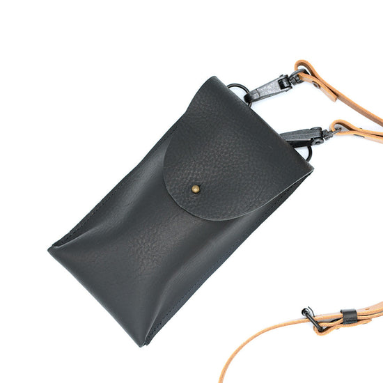 Top view of black dive bag with a golden rivet closure and the tan strap just visible behind and going out of the photograph on the right.