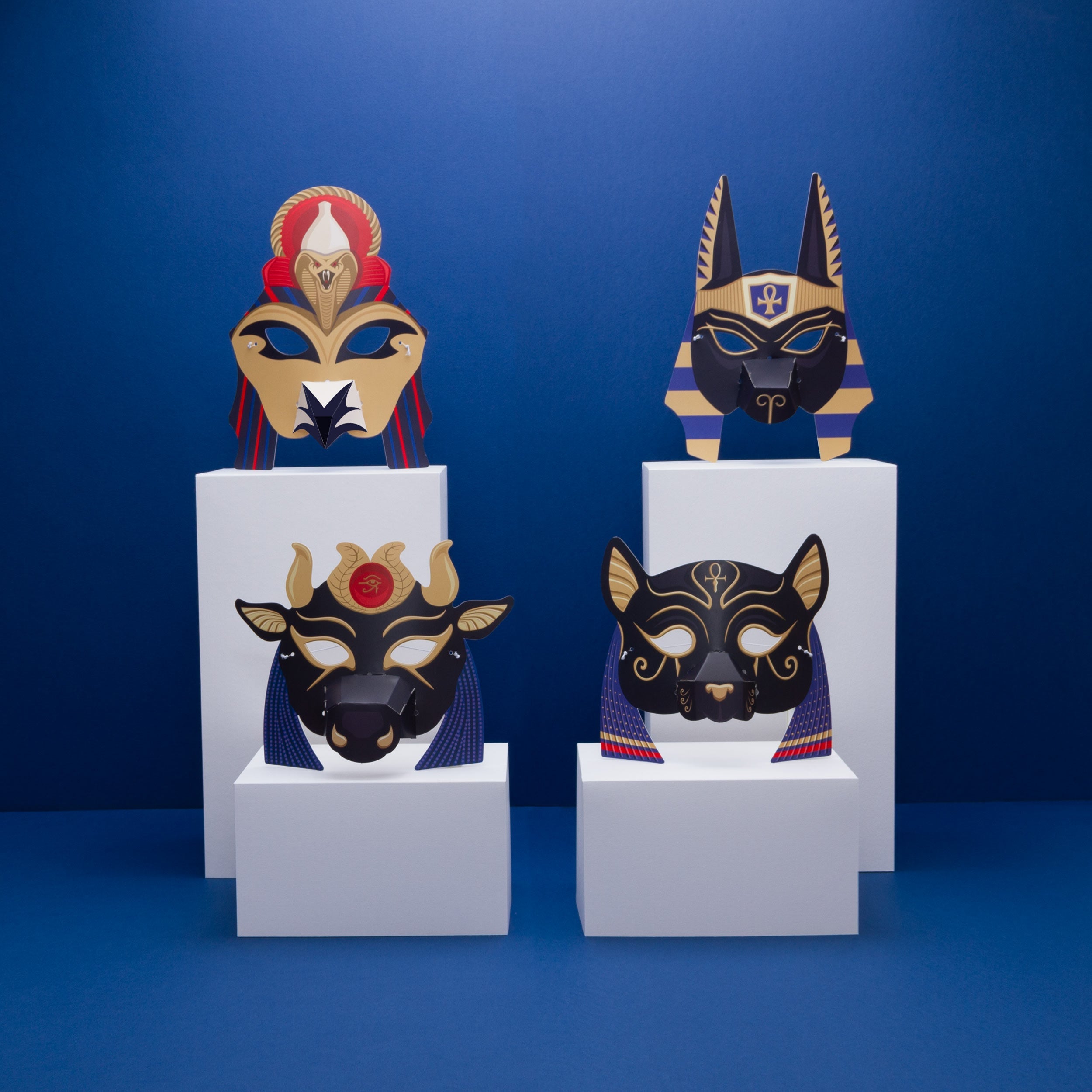 All four masks on four white rectangle pedestals. Hathor and Bastet are at the front and lower with Horus and Anubis at the bakc and on taller pedestals.
