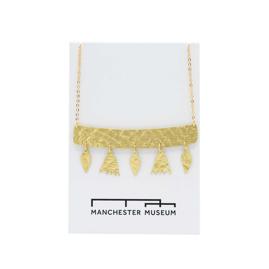 Hammered brass bar necklace with five flower shaped pendants suspended from the bottom of the bar. Presented on a white, museum branded backing card.