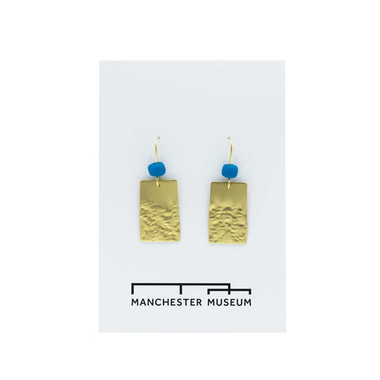 Brass rectangular pendant earrings with a turquoise glass bead on the hoop over the rectangles. Presented on a white, museum branded backing card.