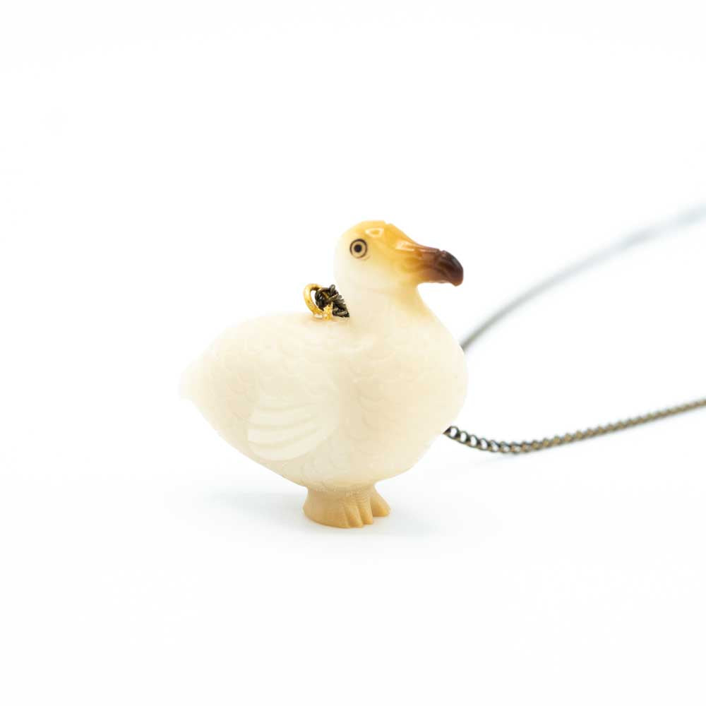 Tagua carved dodo which is mostly white with some brown on the face and faint yelow on the feet. The chain is out of focus in the background.