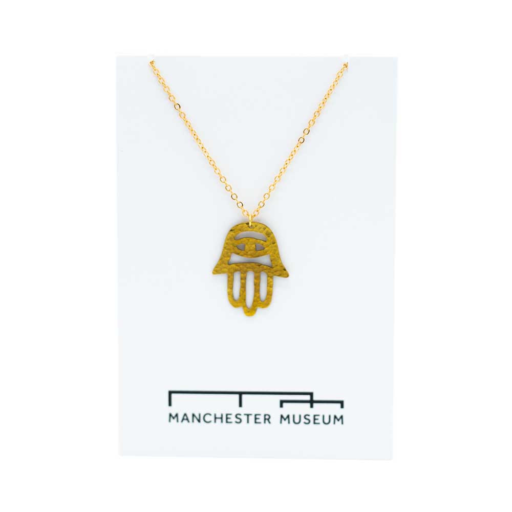 Load image into Gallery viewer, Fatima hand brass necklace draped over the white museum branded card that is part of the sustainable packaging.
