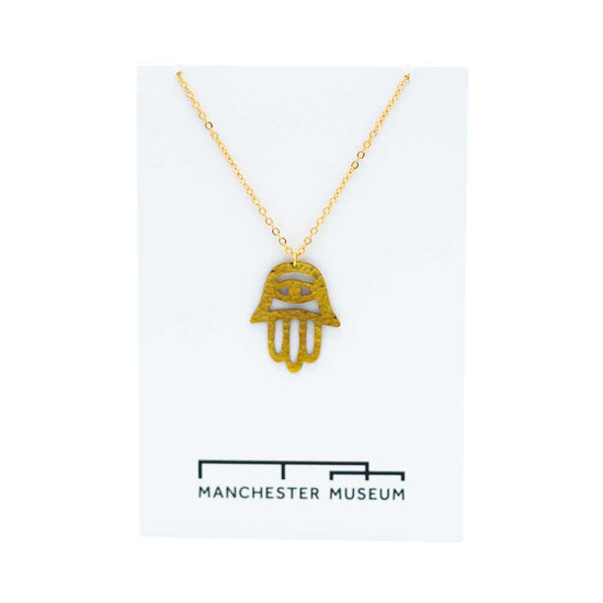 Load image into Gallery viewer, Fatima hand brass necklace draped over the white museum branded card that is part of the sustainable packaging.
