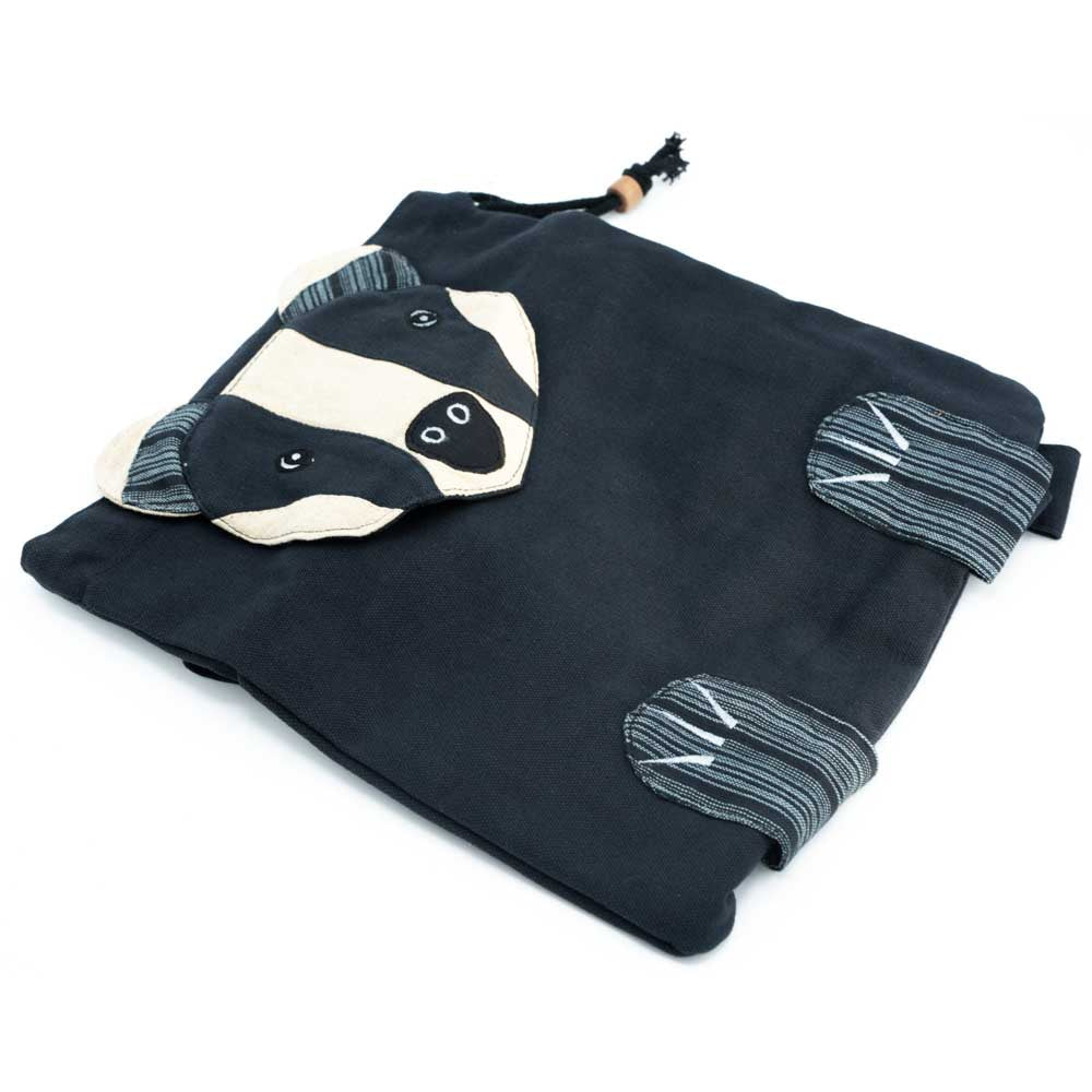 Load image into Gallery viewer, The black badger backpack with a badger face shaped closure flap and little feet attached on the bottom. Slightly angled side view.
